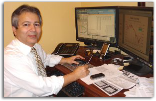 Kamran Afshar, Ph.D. at his desk, working at a computer with economic charts on screen